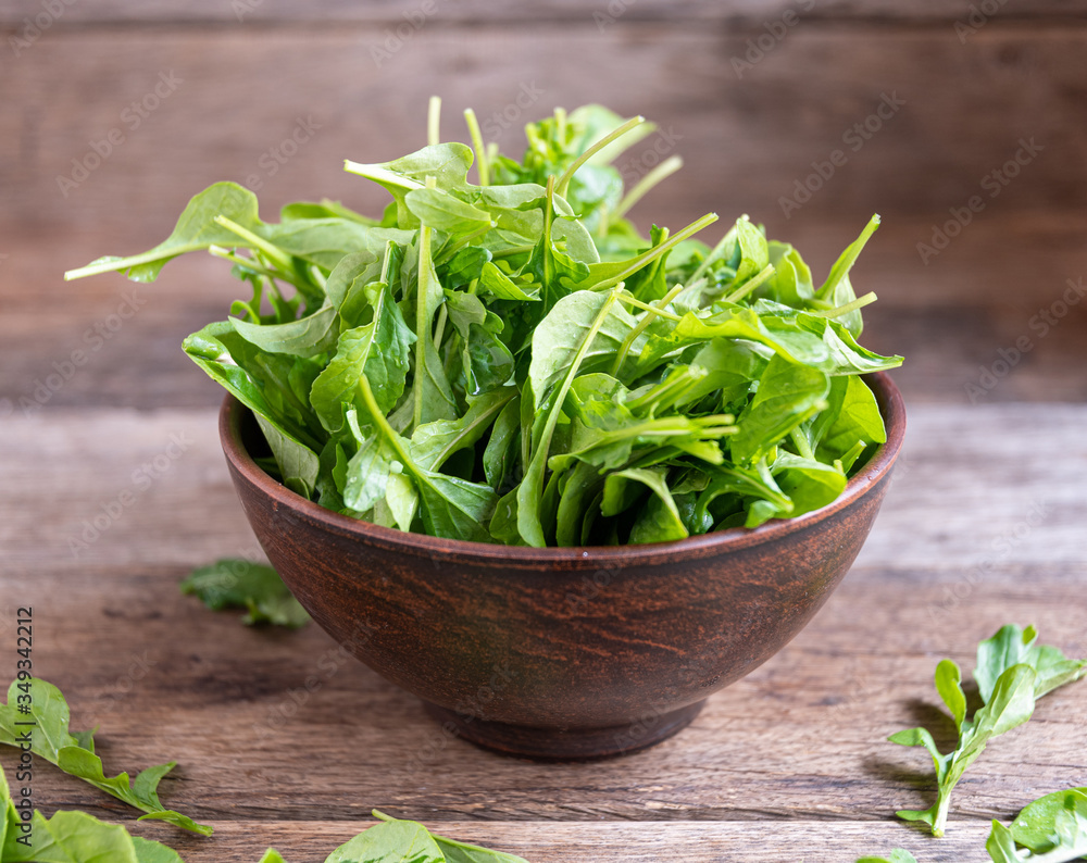 Fresh, ripe arugula in a clay bowl on a wooden table. Fresh, ripe arugula in a clay bowl on a wooden table.