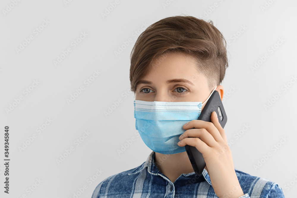 Girl with a mobile phone in a medical mask and a blue plaid shirt. Short hairstyle, European, caucasian woman on a gray background. Girl with a mobile phone in a medical mask and a blue plaid shirt. Short hairstyle, European, caucasian woman on a gray background.