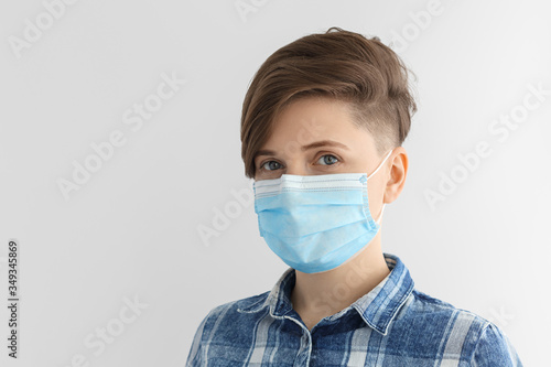 Girl in a medical mask and a blue plaid shirt. Short hairstyle, European, caucasian woman on a gray background.