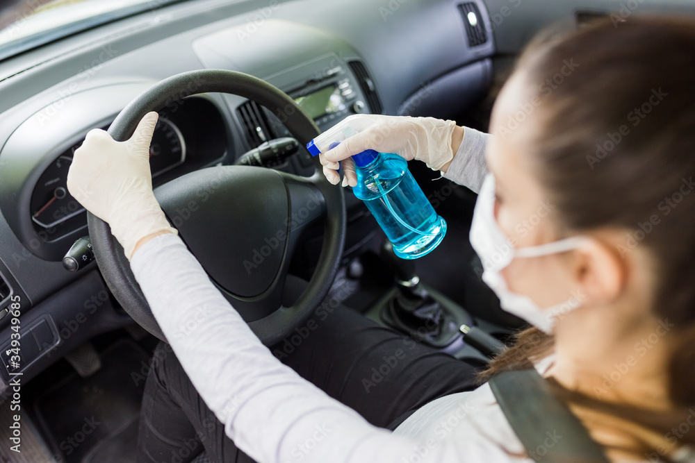 Woman with face mask and rubber gloves using spray bottle sanitizer to protect car steering wheel from bacteria. Antiseptic, hygiene and healthcare concept. Woman with face mask and rubber gloves using spray bottle sanitizer to protect car steering wheel from bacteria. Antiseptic, hygiene and healthcare concept.