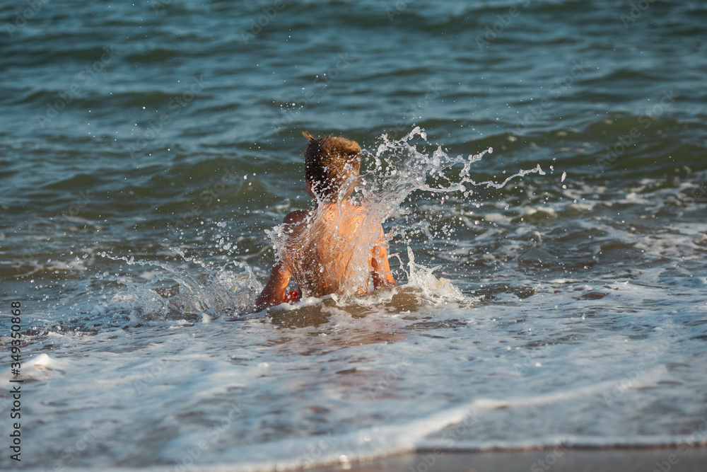 Fototapeta premium verano en la playa niño que salta y cae al agua del mar olas
