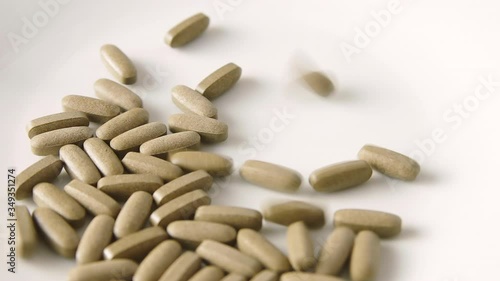 Herbal medicine tablets (black walnut leaves) fall onto a white plate and scatter. Concept for self-medication, natural medicine and dangers of overdose
