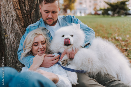 Fototapeta Naklejka Na Ścianę i Meble -  Smiling young man hugging his girlfriend and dog outdoors