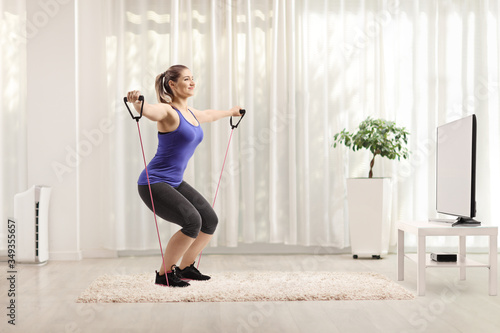 Young female exercising with a resistance band while watching tv
