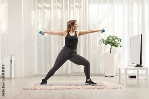 Corpulent woman exercising with dumbbells in front of a tv