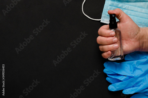 Hand sanitizer bottle in hand, medical mask, medical gloves on black background. Antibacterial liquid against 19-ncov. Stop coronavirus concept. Using antibacterial gel for hands during quarantine.