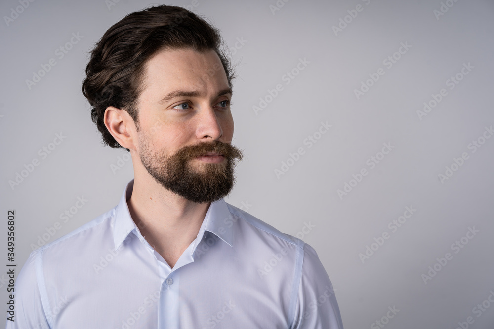 Portrait of young man with beard in white shirt, he smiles and looks away Portrait of young man with beard in white shirt, he smiles and looks away
