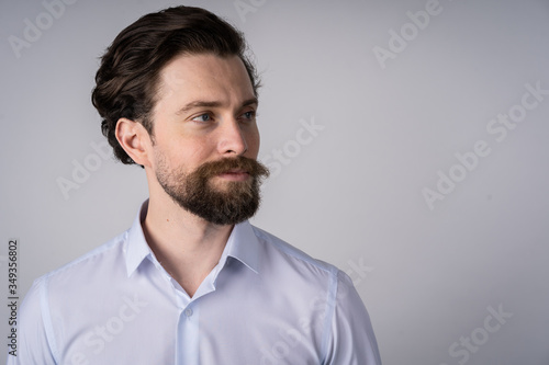 Portrait of young man with beard in white shirt, he smiles and looks away