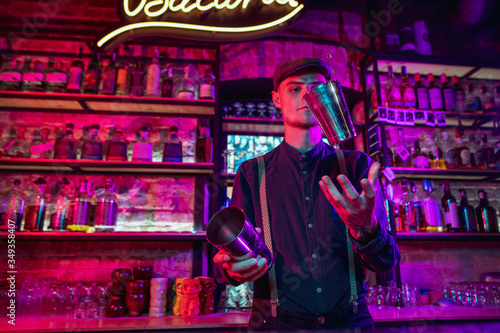 Professional barman finishes preparation of alcoholic cocktail for guest in multicolored neon light. Entertainment, drinks, service concept. Modern bar, crafted beverages, trendy neoned colors.