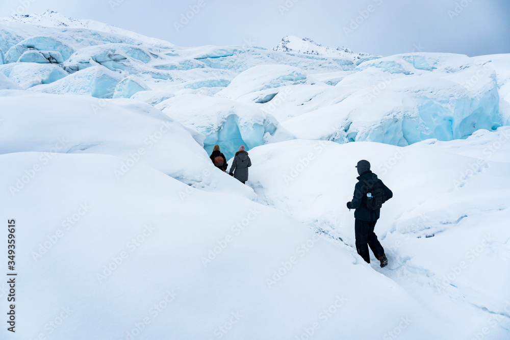 Group of three hikers trekking on the snow in Matanuska Glacier, Alaska. They are following a path into the ice caves. Extreme adventure during winter holidays. Having fun in the mountains. 