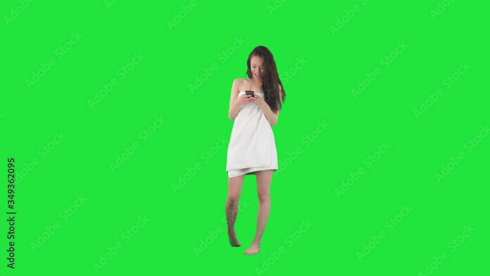 Happy young relaxed woman in bathroom towel using phone texting with friends. Full body isolated on green screen background. Happy young relaxed woman in bathroom towel using phone texting with friends. Full body isolated on green screen background.