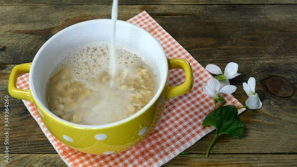 Healthy breakfast with porridge. Milk is added to oatmeal porridge in yellow bowl. On kitchen table. Close-up. Healthy breakfast with porridge. Milk is added to oatmeal porridge in yellow bowl. On kitchen table. Close-up.