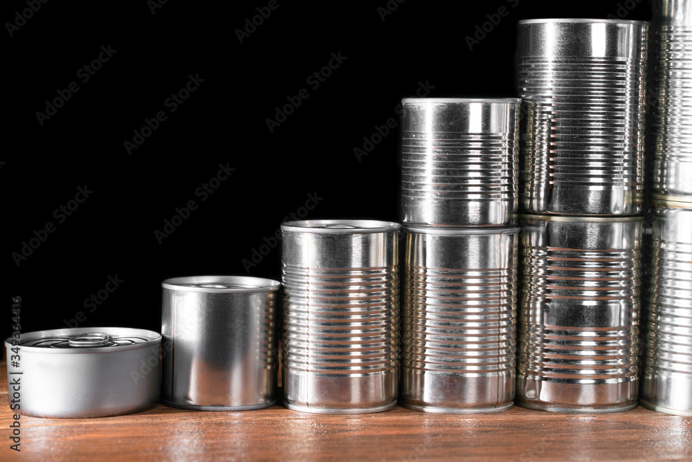 Small and medium canned products in silver pyramid on brown wooden table and dark background Small and medium canned products in silver pyramid on brown wooden table and dark background