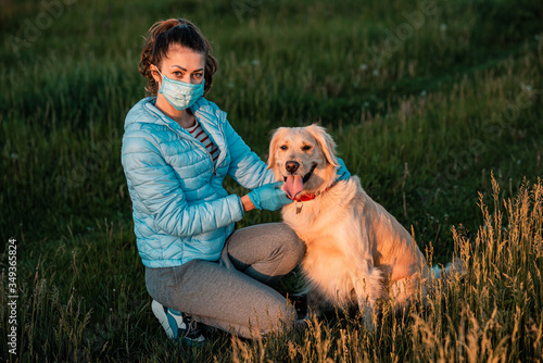 Girl trying to protect big Golden retriever dog from a coronavirus with a medical mask in nature park. Protection against disease during epidemics and pandemics. Covid-19