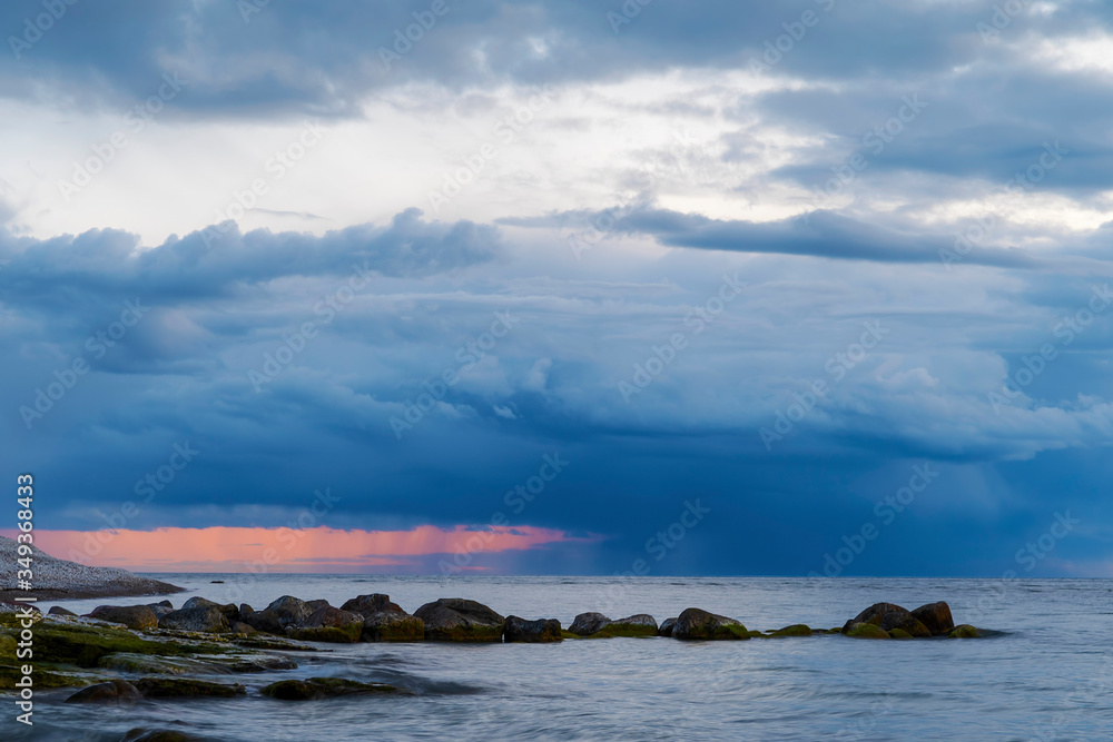 sunset storm clouds over ocean with boulders in foreground