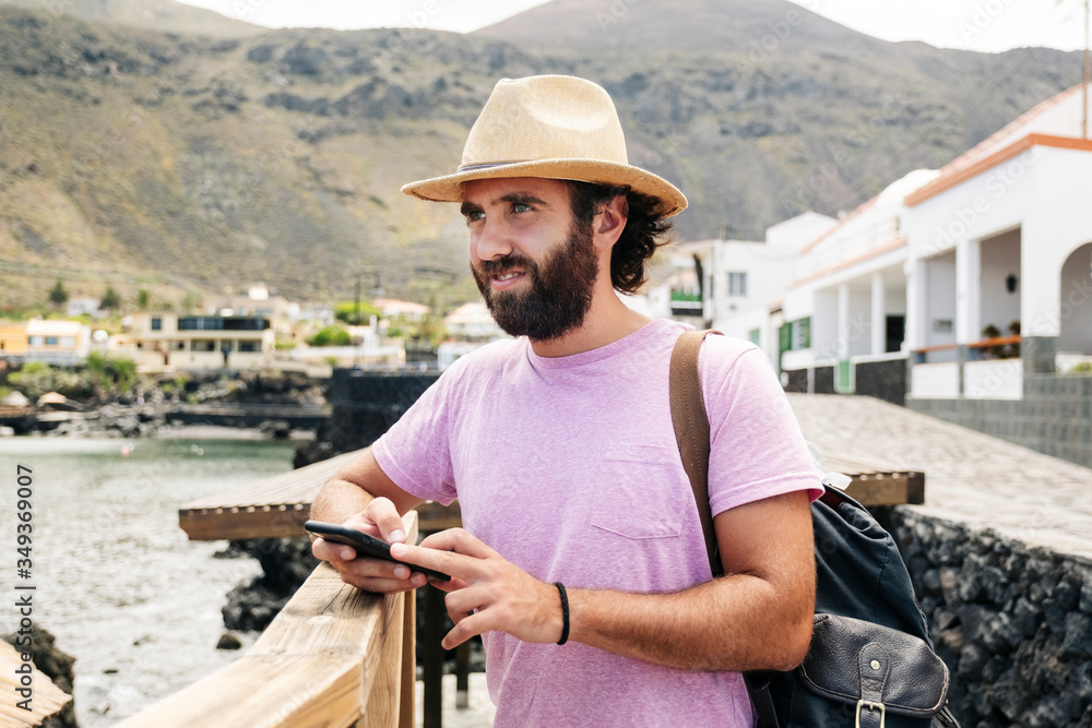 A tourist man with hat and backpack uses the mobile phone in a coastal town El Hierro, Canary Islands