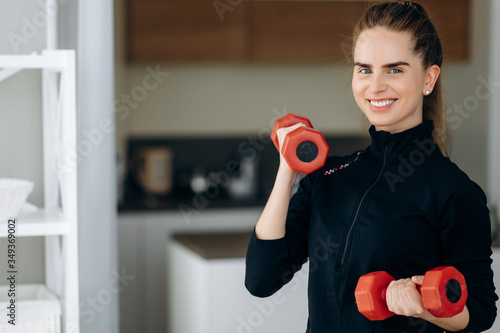 Sport at home. Beautiful athletic positive girl in sportswear does sports at home, she does exercise with dumbbells