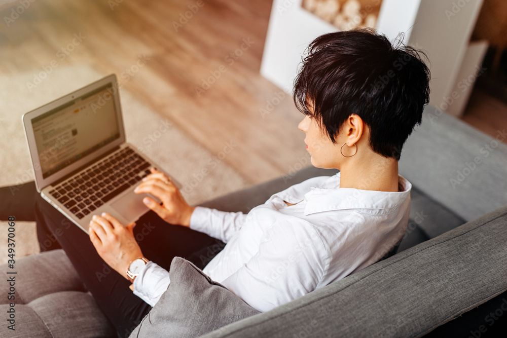 Happy casual beautiful woman working on a laptop sitting on the sofa in the house, photo from above Happy casual beautiful woman working on a laptop sitting on the sofa in the house, photo from above