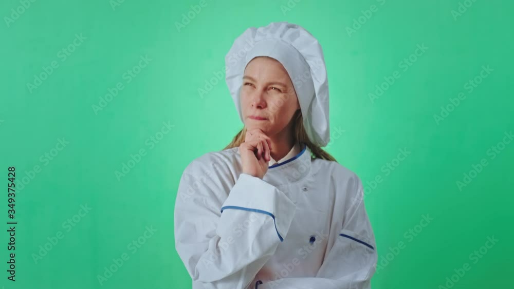 Woman baker in the uniform in front of the camera green wall background have a serious think face she try to get a new recipe for her cake very charismatic face chroma key concept Woman baker in the uniform in front of the camera green wall background have a serious think face she try to get a new recipe for her cake very charismatic face chroma key concept