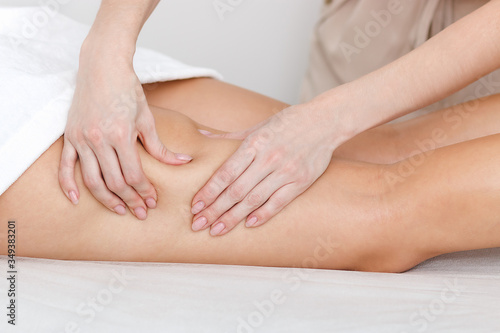 Young woman massage therapist makes hands anti-cellulite procedures on the skin of the hips of a girl in a medical center. Beautiful legs close-up. Bright studio shot for a beauty salon.