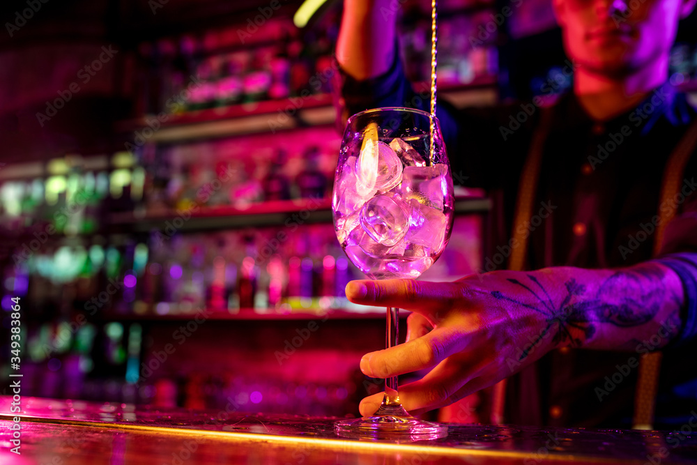 Close up of professional barman finishes preparation of alcoholic cocktail in multicolored neon light, gives it to client. Entertainment, drinks, service concept. Modern bar, trendy neoned colors. Close up of professional barman finishes preparation of alcoholic cocktail in multicolored neon light, gives it to client. Entertainment, drinks, service concept. Modern bar, trendy neoned colors.