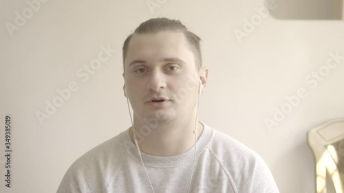 Portrait of young handsome man talking at camera. Close-up of brunette Caucasian guy in earphones chatting in online conference. Remote work, Covid-19 lockdown. S-log2, QuickTime ProRes 422 HQ. photo