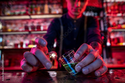 Close up of professional barman finishes preparation of alcoholic cocktail in multicolored neon light, gives it to guest. Entertainment, drinks, service concept. Modern bar, trendy neoned colors.