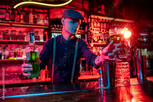 Professional barman proposing alcoholic cocktails, shots, beverages to guest in multicolored neon light. Entertainment, drinks, service concept. Modern bar, crafted beverages, trendy neoned colors.