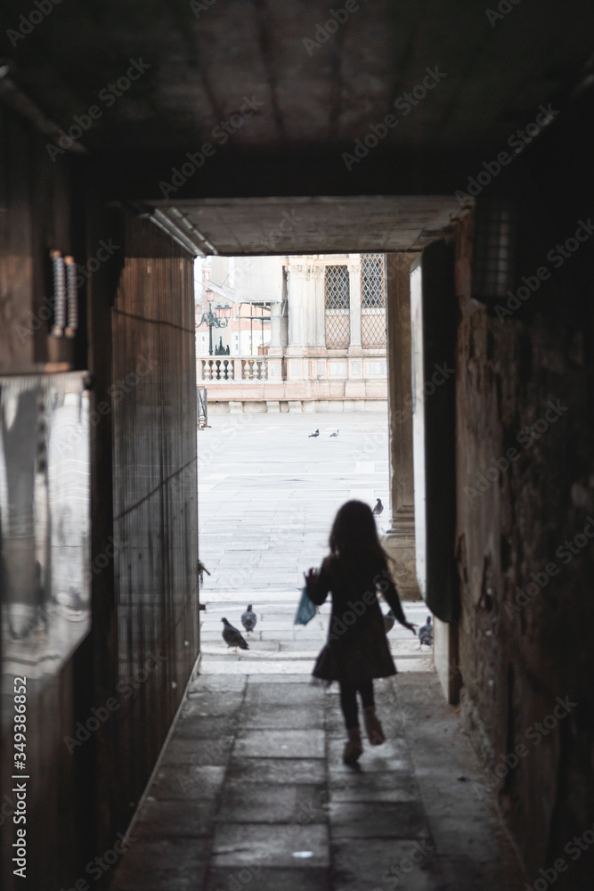 rear view of a little girl running towards the saint mark's square in Venice italy,she is holding a surgical mask in her hand