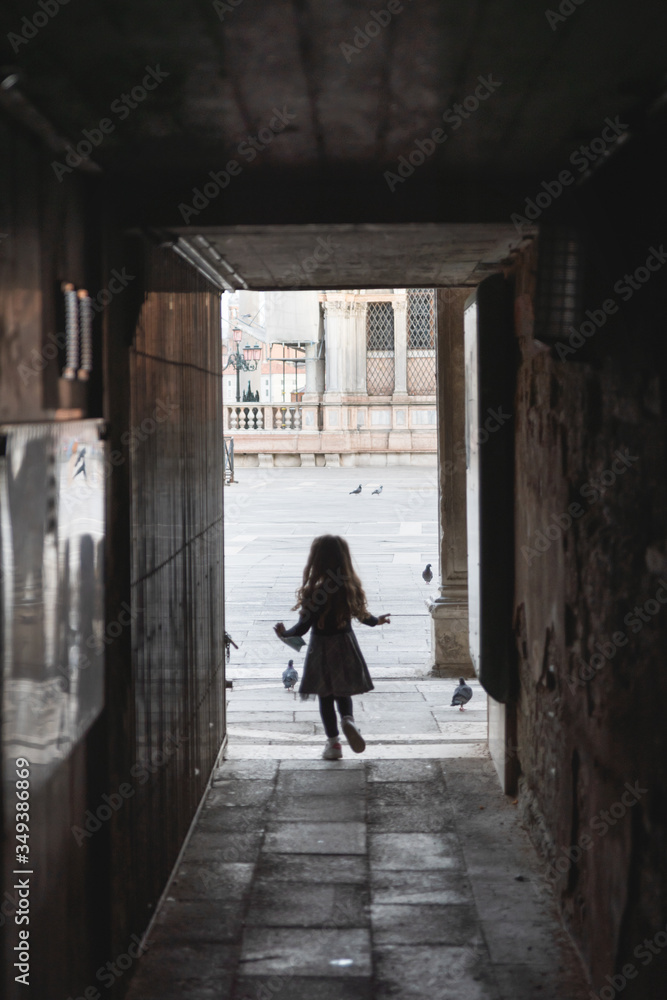 rear view of a little girl running towards the saint mark's square in Venice italy,she is holding a surgical mask in her hand