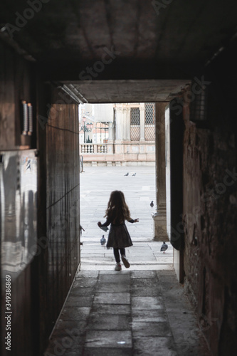 rear view of a little girl running towards the saint mark's square in Venice italy,she is holding a surgical mask in her hand