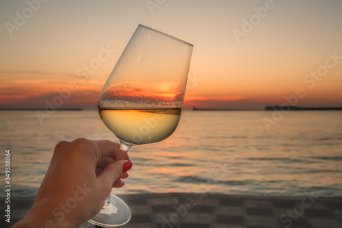A glass of wine in a woman's hand against the background of the sea. Summer sunset by the sea. A glass of white wine.