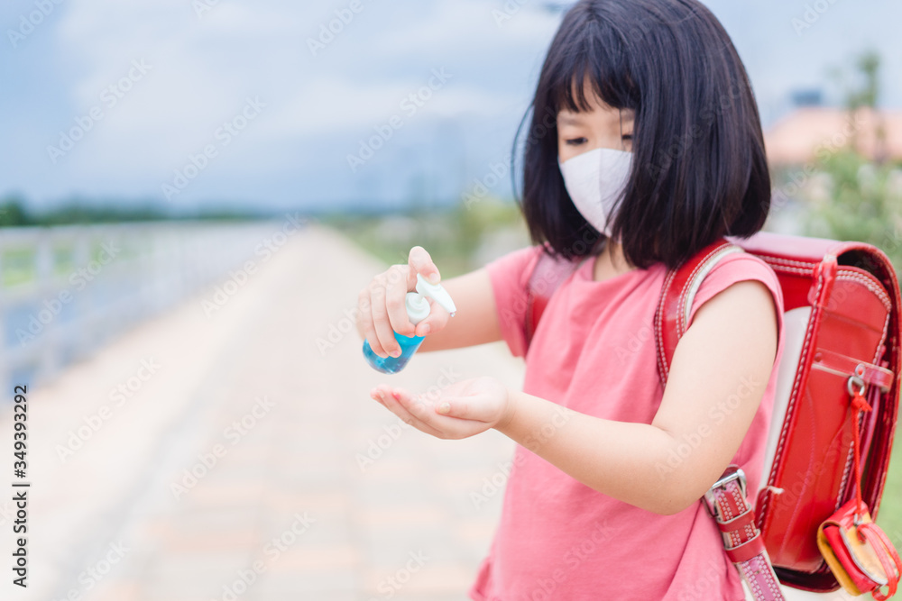Asian kid girl student wearing face mask applying alcohol hand gel.Mini sanitizer pump.Reopen school from lockdown. Back to school.Covid-19 coronavirus pandemic.New normal lifestyle.Education concept Asian kid girl student wearing face mask applying alcohol hand gel.Mini sanitizer pump.Reopen school from lockdown. Back to school.Covid-19 coronavirus pandemic.New normal lifestyle.Education concept