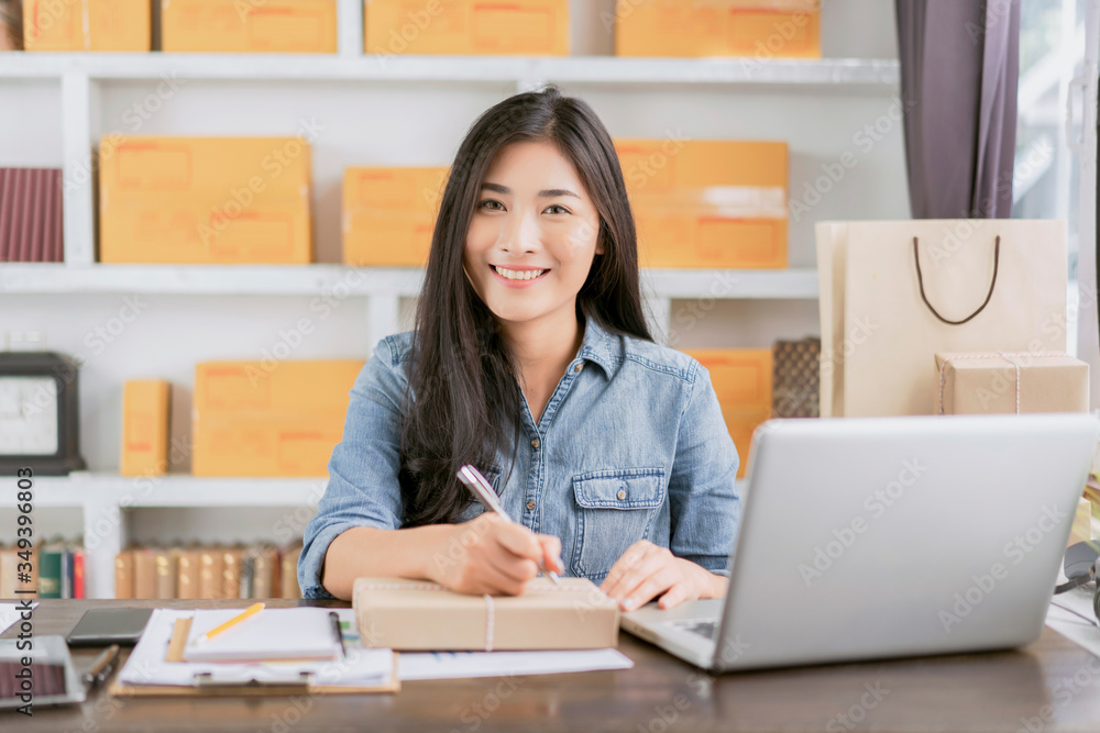 beautiful Asian businesswoman smiling using writing on parcel packaging, using computer laptop ecommerce online store selling delivering products, working at home office during quarantines isolation beautiful Asian businesswoman smiling using writing on parcel packaging, using computer laptop ecommerce online store selling delivering products, working at home office during quarantines isolation