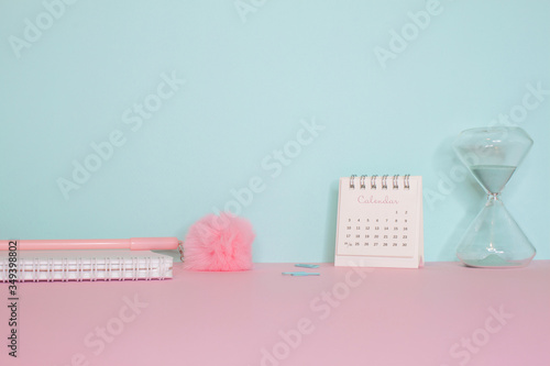 Side view on a still life. Pink fluffy pen, notepad and calendar on a pink table. Turquoise wall on the back