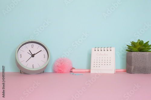 Side view on a still life. Pink fluffy pen, clock and calendar on a pink table. Turquoise wall on the back