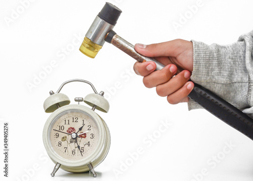 Poor time management concept. Close up a hand is holding a hammer and a desk clock over white background.