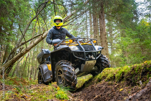 A man in a yellow helmet rides a Quad bike through the woods. Quad bike on a forest road. Journey through the forest on a Quad bike. Sale and rental of ATVs. Driving on bad roads. photo