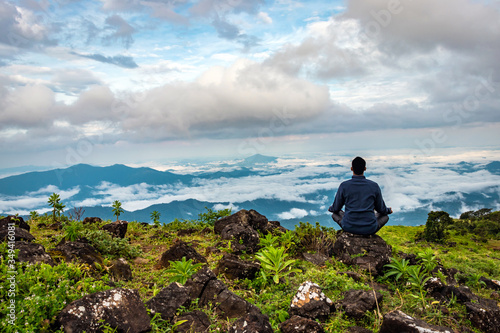 man meditating on rock isolated at the serene nature with amazing cloud layers in foreground