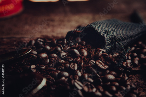 closeup of coffee beans and grounds spilling out of a small, black sack onto a wooden table