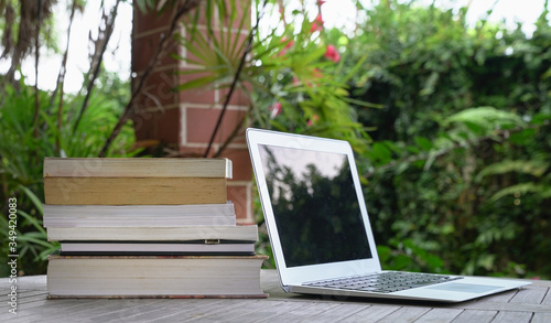 Φωτογραφία Stacked of books next to computer laptop. Garden view.