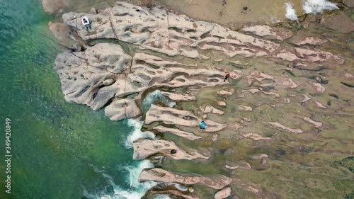 Aerial view of Hikers crossing over rocky waterfall at Austin, Texas swimming hole zoom out photo