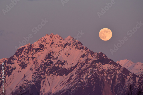 Photo Alpenglow colors the full moon rising over Alaska's Chugach Range