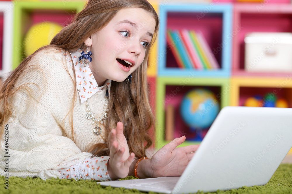 Emotional cute girl using laptop while lying on green floor at home Emotional cute girl using laptop while lying on green floor at home