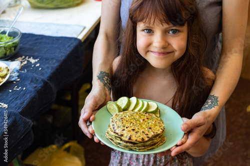 Mother and girl hold vegan food in hands together - flatbread and zucchini. Family care and healthy meal concept.