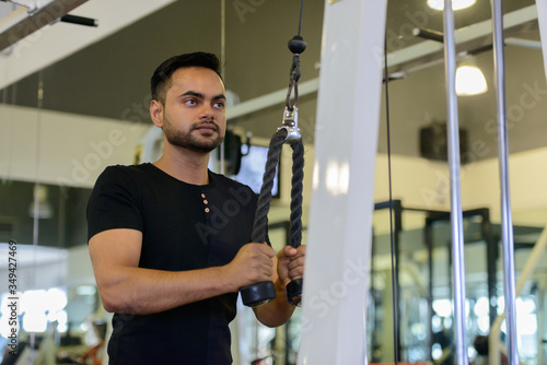 Young bearded Indian man using exercise equipment at the gym