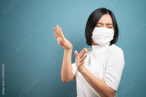 Don't touch me. Asian woman wearing hygiene mask panic and disguted showing hand stop sign and standing isolated over blue background. Health care concepts.