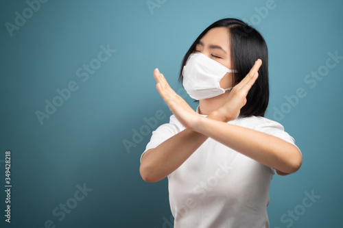Asian woman wearing hygiene mask showing arms crossed stop sign and standing isolated over blue background. Health care concepts.