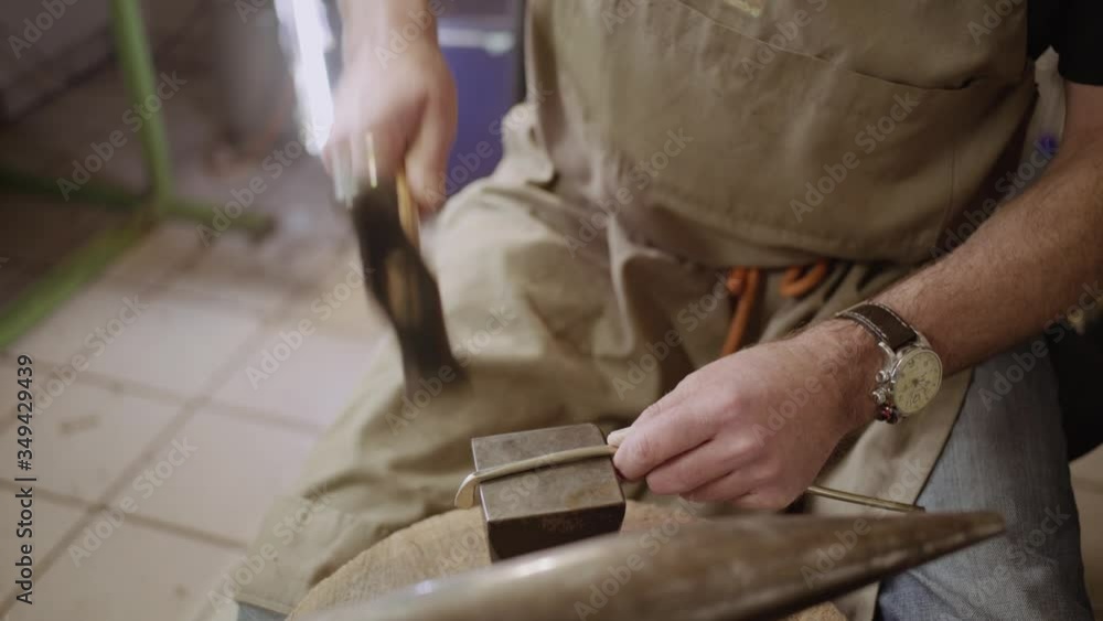 Instrument maker hammering metal bar into shape on anvil to forge a flute key for a transverse flute. Instrument maker hammering metal bar into shape on anvil to forge a flute key for a transverse flute.