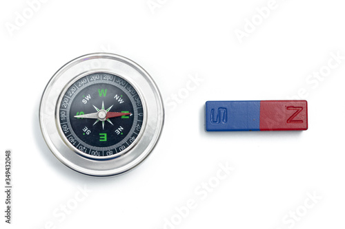 Close up analog compass and bar magnet over white background. South pole of the magnet effect on the compass needle. For education purpose. 